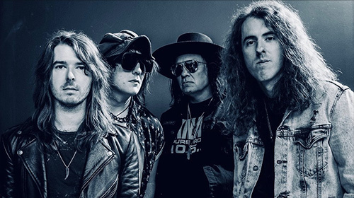 Four male rock musicians posing together for a promo photo in dark outfits, leather jackets, and sunglasses (band portrait).