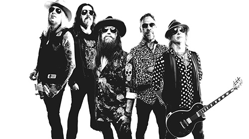 Five-member rock band posing together, black-and-white photo with guitars and sunglasses.